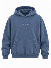 Front view of the Ocean Mark washed blue embroidered hoodie with three small cream satin-stitch waves at the center chest